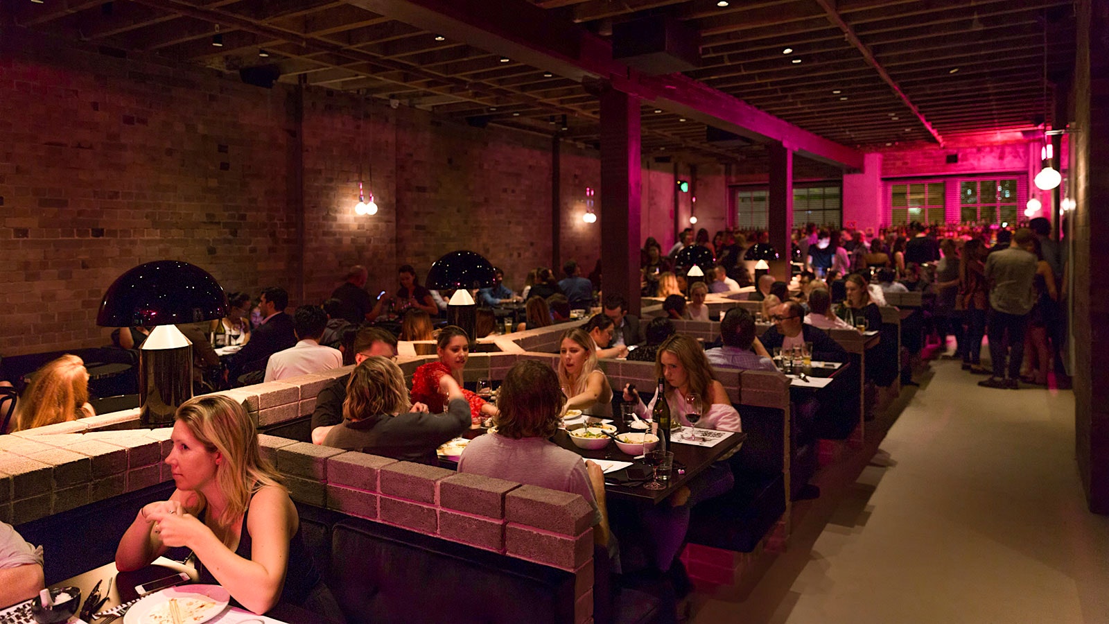 People eating in the dining room of Chin Chin Sydney, where pink lights shine on the walls